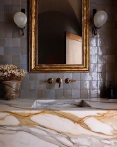 a bathroom with marble counter tops and gold framed mirror