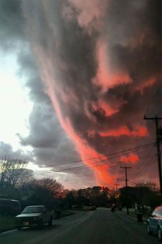 the sky is filled with clouds and cars are parked on the side of the road