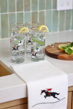 two glasses with water and lemons sitting on a counter next to a cutting board