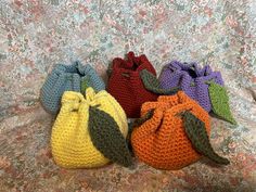 four crocheted bags sitting on top of a floral print bed spread, each containing an orange, yellow, green, and purple bag