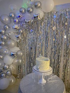 a white cake sitting on top of a table next to silver foil balloons and streamers