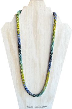 a multicolored beaded necklace is displayed on a wooden display stand with a white background