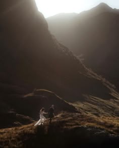 a bride and groom walking up a hill in the mountains at their wedding day with sun shining down on them