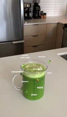 a green smoothie in a glass on a kitchen counter with the ingredients labeled below