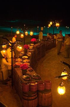 an outdoor dinner setup on the beach at night with candles and lanterns in the dark