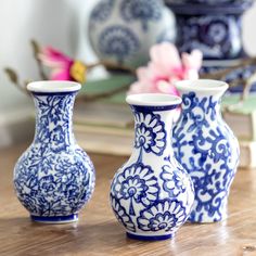 three blue and white vases sitting on top of a wooden table next to flowers