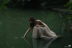 a woman is sitting in the water with her hands on her knees and looking down