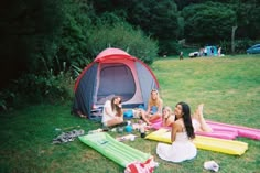 three women sitting on inflatable mattresses next to a tent and picnic table