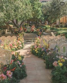 rows of chairs are lined up in the middle of an outdoor area with flowers and greenery