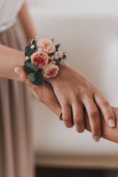 two people holding hands with flowers on their wrist and one person's hand in the other