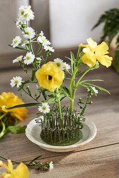 yellow and white flowers sitting in a vase on a wooden table with grass growing out of it