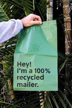 a person holding a green bag that says hey i'm a 100 % recycled mailer