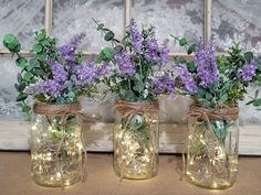 three mason jars filled with purple flowers and fairy lights