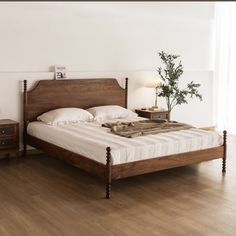 a bed sitting on top of a wooden floor next to a night stand with a plant