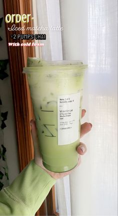 a person holding up a green drink in front of a window with the words order on it