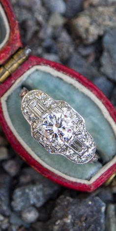 an antique diamond ring sits in its box on the ground next to some rocks and stones