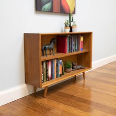 a wooden book shelf with books on top of it next to a painting and potted plant