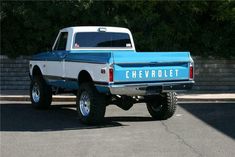 a blue and white pickup truck parked in a parking lot next to a brick wall