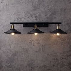 three lights are hanging on the wall in front of a concrete wall with a black pipe