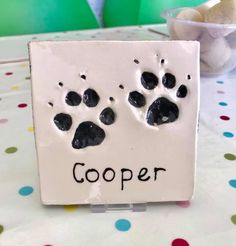 a white sign with black paw prints and the word cooper written on it next to a teddy bear