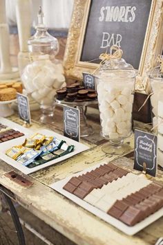 a table topped with lots of desserts and candies next to a chalkboard sign