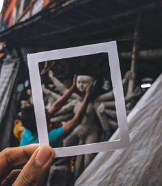 a person holding up a square photo in front of a building with statues on it