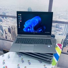 an open laptop computer sitting on top of a table next to a window with cityscape in the background