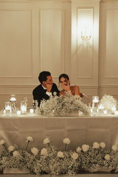 a bride and groom are sitting at a table with candles in front of their faces