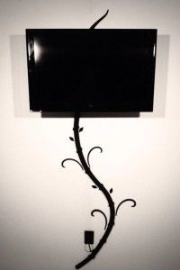 a tv mounted to the side of a wall with a plant growing out of it