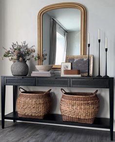 a console table with two baskets on it and a large mirror in the corner behind it