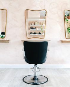 a hair salon chair in front of two mirrors and shelves with bottles on the wall