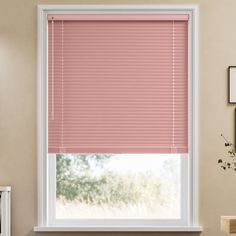 a window with pink blinds in the corner and a white frame on the wall next to it