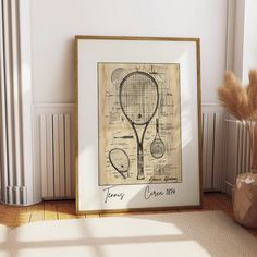 a framed drawing of a tennis racquet on the floor next to a vase