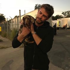 a man holding a dog in his right hand while standing on the side of the road