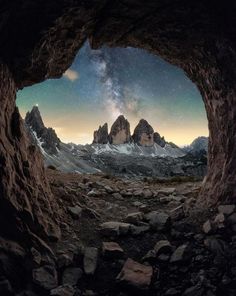 an image taken from the inside of a cave looking at mountains and stars in the sky