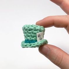 a hand holding a small green crochet hat with a price tag on it