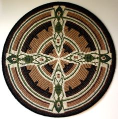 a woven wall hanging in the shape of a cross with green and brown designs on it