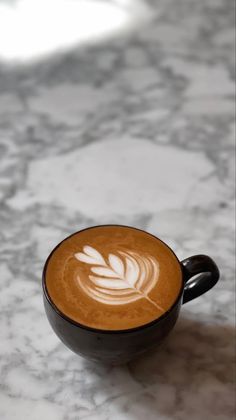 a cappuccino with a leaf on it sits on a marble countertop