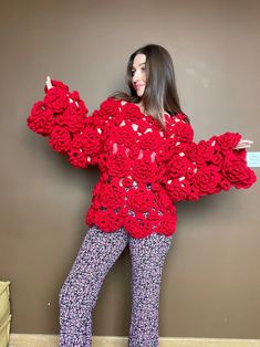 a woman is standing in front of a wall wearing red crocheted sweater and pants