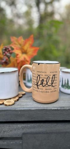 two coffee mugs sitting on top of a table with autumn leaves in the background