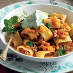 a white bowl filled with pasta and meat covered in sour cream, garnished with mint