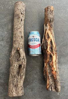 a can of beer sitting next to two pieces of driftwood on a cement floor