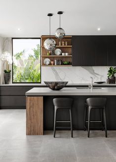 a modern kitchen with black cabinets and marble counter tops, two bar stools at the island