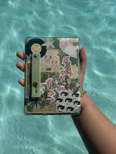 a person holding up a small case with stickers on it in front of the water