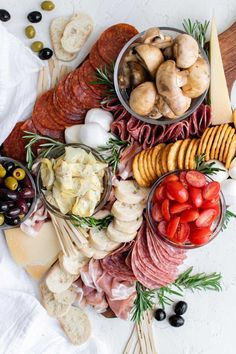 an assortment of meats and cheeses on a platter with olives, tomatoes, mushrooms, bread sticks