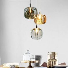 three lights hanging from the ceiling above a table with plates and bowls on it,