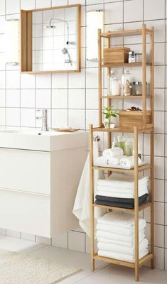 a bathroom with white tiled walls and flooring, including a wooden shelf that holds folded towels