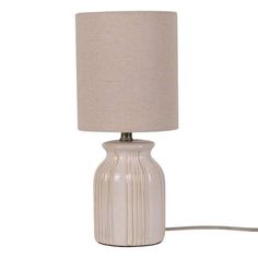 a white table lamp with a beige shade on the base and a cord attached to it