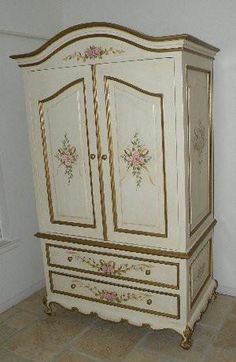 a white armoire with flowers painted on the doors and drawers in an empty room