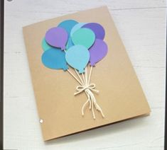 a brown card with blue, purple and green balloons tied to it on a white table